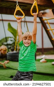 Cute Young Boy In Green Shirt And Black Shorts Is Playing On Back Yard Playground. 