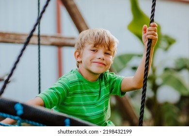 Cute Young Boy In Green Shirt And Black Shorts Is Playing On Back Yard Playground. 