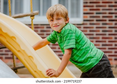 Cute Young Boy In Green Shirt And Black Shorts Is Playing On Back Yard Playground. 