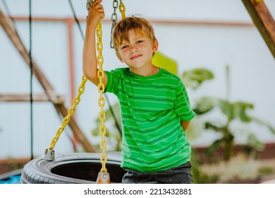 Cute Young Boy In Green Shirt And Black Shorts Is Playing On Back Yard Playground. 