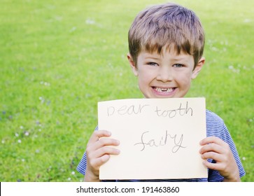 Cute Young Boy With A Missing Tooth Holding A Sign For The Tooth Fairy