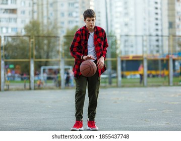 Cute Young Boy Plays Basketball On Street Playground. Teenager In Red Check Flannel Shirt With Orange Basketball Ball Outside. Hobby, Active Lifestyle, Sport Activity For Kids.