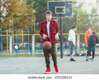 Cute Young Boy Plays Basketball On Street Playground. Teenager In Red Flannel Checked Shirt With Orange Basketball Ball Outside. Hobby, Active Lifestyle, Sport Activity For Kids.