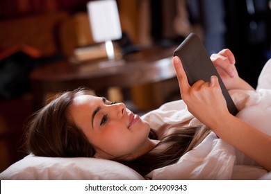 Cute young brunette  using tablet computer laying in bed. - Powered by Shutterstock