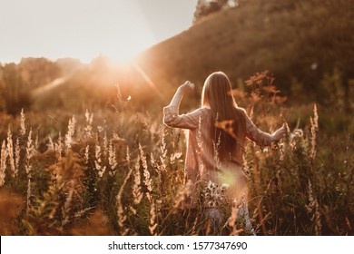 Cute young caucasian girl with long fluffy hair in a field at sunset. Beautiful young woman with brown hair dancing in a field at sunset. Freedom and nature concept.Soft focus - Powered by Shutterstock