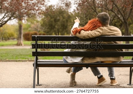 Cute young couple hugging while sitting on bench in autumn park, back view