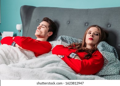Cute, young couple lying in bed, looking angry with each other. Relationship problems