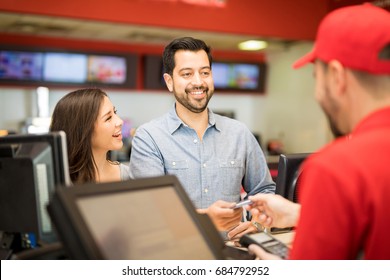 Cute Young Couple At The Movie Theater While The Man Pays For The Tickets With A Credit Card At The Box Office