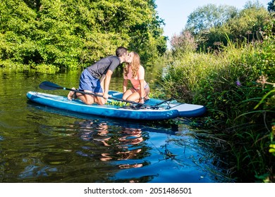 Cute Young Couple Paddle Boarding In A Beautiful River