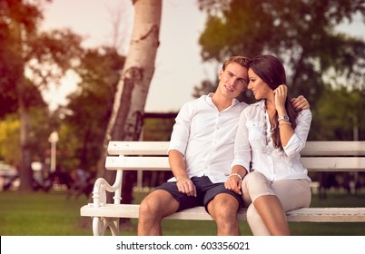 Cute Young Couple Sitting At Park On The Bench