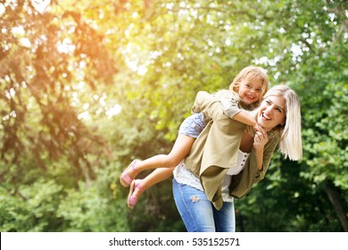 Cute young daughter on a piggy back ride with her mother. Looking at camera. - Powered by Shutterstock