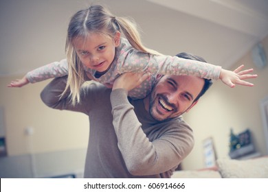 Cute Young Daughter On A Piggy Back Ride With Her Dad. Looking At Camera.