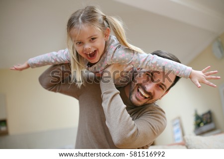 Cute young daughter on a piggy back ride with her dad. Looking at camera.
