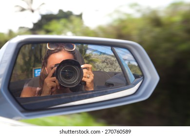 Cute young female photographer with camera. Woman reflected in the rearview mirror of a car on a summer day (out of focus). - Powered by Shutterstock