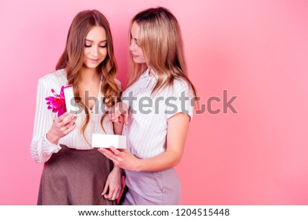 cute and young female teenager person daughter gives a Christmas box with a gift to mom on a pink background in studio . concept of celebrating new year 2019 family with presents