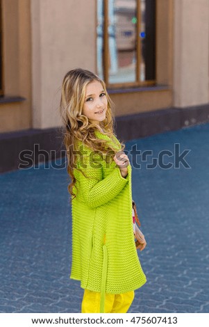 cute young girl with curly hair in a green cardigan is looking at you