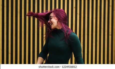 Cute Young Girl Dancing On Background Of Simple Geometric Pattern. Girl Has Eggplant Hair Flying In Motion. She Is In Dark Green Dress. Pleasure And Ecstasy Of Dance