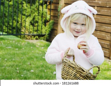 Cute Young Girl Dressed In A Pink Bunny Suit Putting An Egg In A Basket