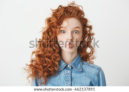 Cute young girl with foxy curly hair making funny face over white background. Copy space.