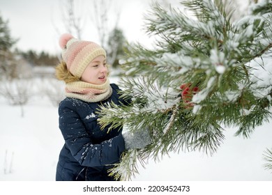 Cute Young Girl Having Fun On A Walk In Snow Covered Park On Chilly Winter Day. Child Exploring Nature. Winter Activities For Kids.