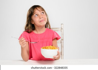 Cute young girl kid holding bowl of breakfast cereal cornflakes looking up, healthy eating and diet concept