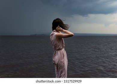 A cute young girl in a pink dress is standing in the water with flying hair during a storm and bad weather. Epic photo. Back view - Shutterstock ID 1517529929