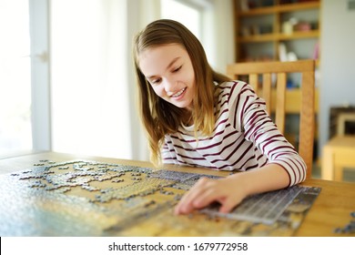 Cute young girl playing puzzles at home. Child connecting jigsaw puzzle pieces in a living room table. Kid assembling a jigsaw puzzle. Fun family leisure. Stay at home activity for kids. - Powered by Shutterstock