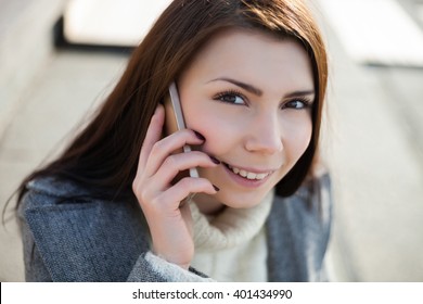 Cute young girl with pug nose talking on the phone at bright spring day outdoors. The model is beautiful and the smart phone is modern