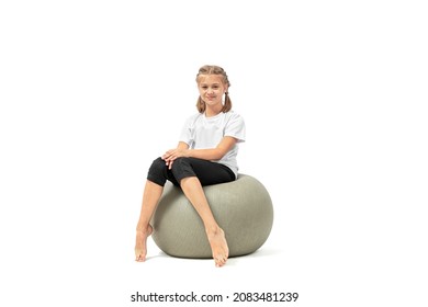 Cute young girl sitting on fitness ball looking at the camera and smiling isolated on white background.
