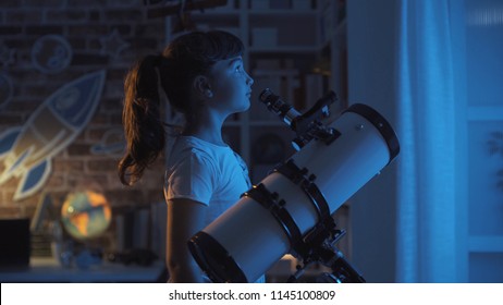 Cute Young Girl Stargazing At Night With A Telescope, She Is Looking Away: Imagination And Childhood Concept