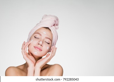 a cute young girl with a towel on her head puts a nourishing cream on her face, her eyes are closed, she enjoys