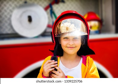 Cute young girl trying on real fireman's helmet standing in front of firetruck.