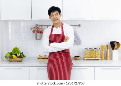 Cute, young and handsome Asian man wearing apron standing and cross arms with self-confident in modern white kitchen. - Powered by Shutterstock