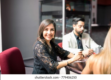 Cute Young Latin Woman Playing Bingo In A Casino With A Group Of Friends And Smiling