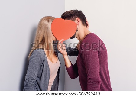 Cute young loving couple is standing and kissing. Their faces are covered by red heart. Isolated