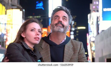 Cute Young Loving Couple In Times Square New York Looking Up At The Bright Billboard Lights. Date Night Location Of New Years Eve Celebration And Ball Drop At Midnight.