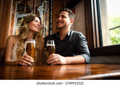 cute and young male and female sitting down at indoor pub having fun and drinking draft beer