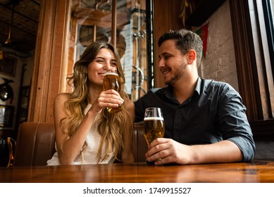 cute and young male and female sitting down at indoor pub having fun and drinking draft beer - Powered by Shutterstock