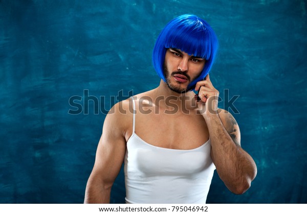 Cute young man wearing blue wig and female cloth.\
Cross dressing male person looking at the camera and talking on the\
phone