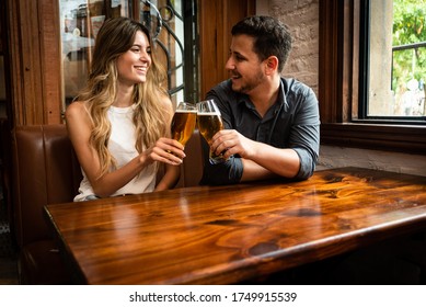 cute and young man and woman friends sitting down at indoor pub having fun toasting and drinking draft beer - Powered by Shutterstock