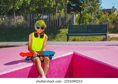 Cute Young Preteen Boy With Green Hair Sit On Ramp Holding Skateboard In City Skatepark