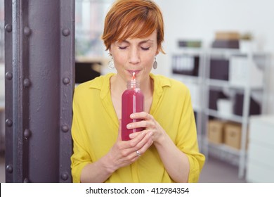 Cute Young Red Haired Woman In Yellow Blouse Standing Up Near Post Taking A Break From Work To Drink Fruit Juice From Bottle And Straw