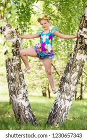 Cute Young Sporty Blond Girl Standing Between Two Birch Trees, Wears Colorfull Sport Swimsuit And Gold Bowler Hat In Sunny Day