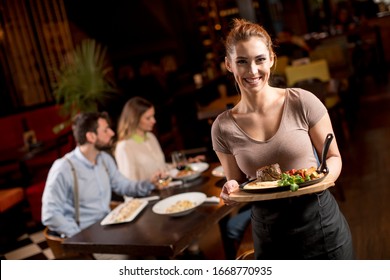 Cute Young Waitress Holding A Wooden Plate With Beef Steak In The Restaurant