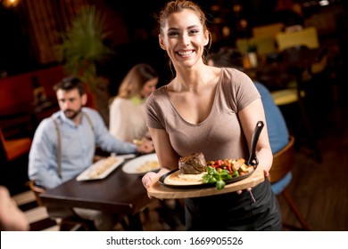 Cute young waitress holding a wooden plate with beef steak in the restaurant - Powered by Shutterstock