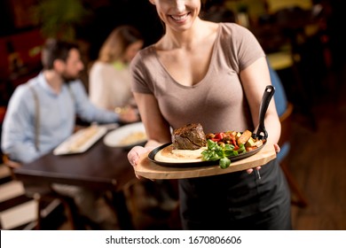 Cute Young Waitress Holding A Wooden Plate With Beef Steak In The Restaurant