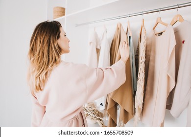Cute young woman in bathrobe standing in front of hanger rack and trying to choose outfit dressing for work or walk. Selection of a wardrobe, stylist, shopping. - Shutterstock ID 1655708509