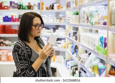 A cute young woman with a cosmetic product in her hands in a cosmetics store.
