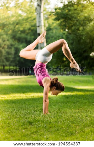Cute young woman doing handstand exercises in the park.