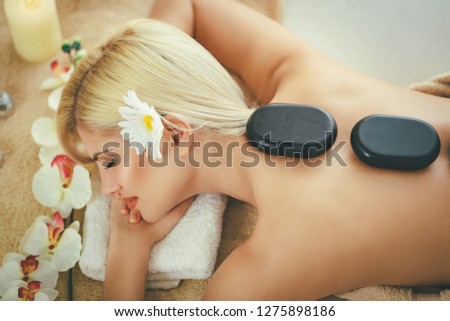 Cute young woman is enjoying during a back massage with warm stones at a spa.